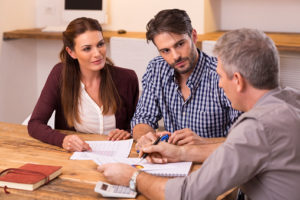 Three people sitting at the table talking with papers in front of them