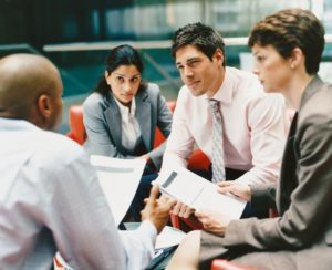 People sitting at a table in a meeting holding papers