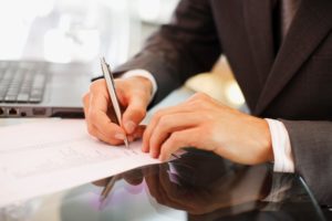 Person signing a paper on a desk with a laptop