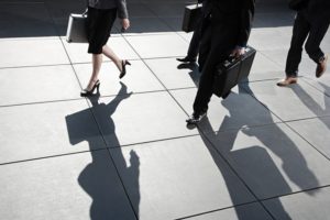 Professionally dressed people walking outside while holding their suitcases